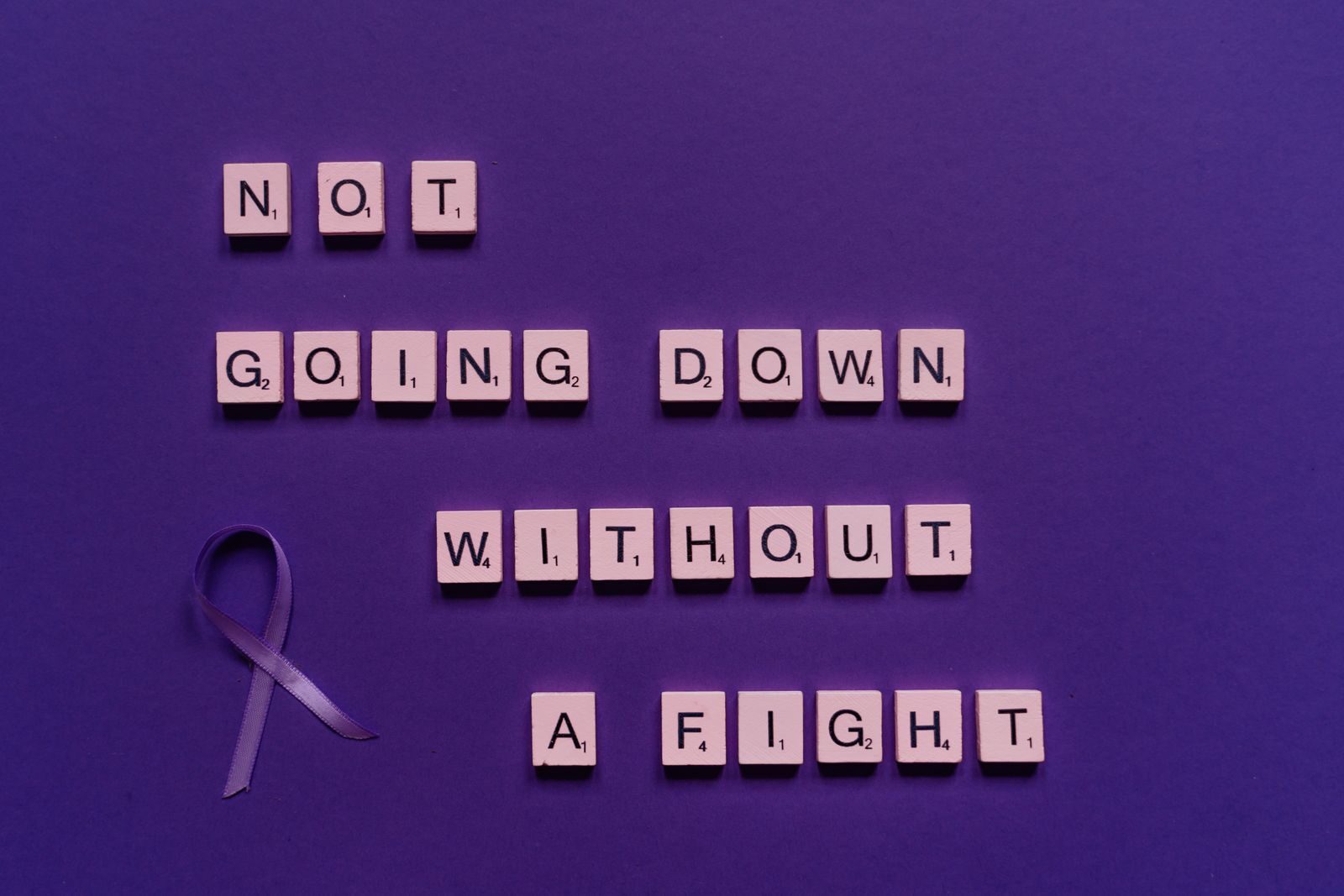 Scrabble tiles with an inspiring quote and a purple ribbon on a purple background.